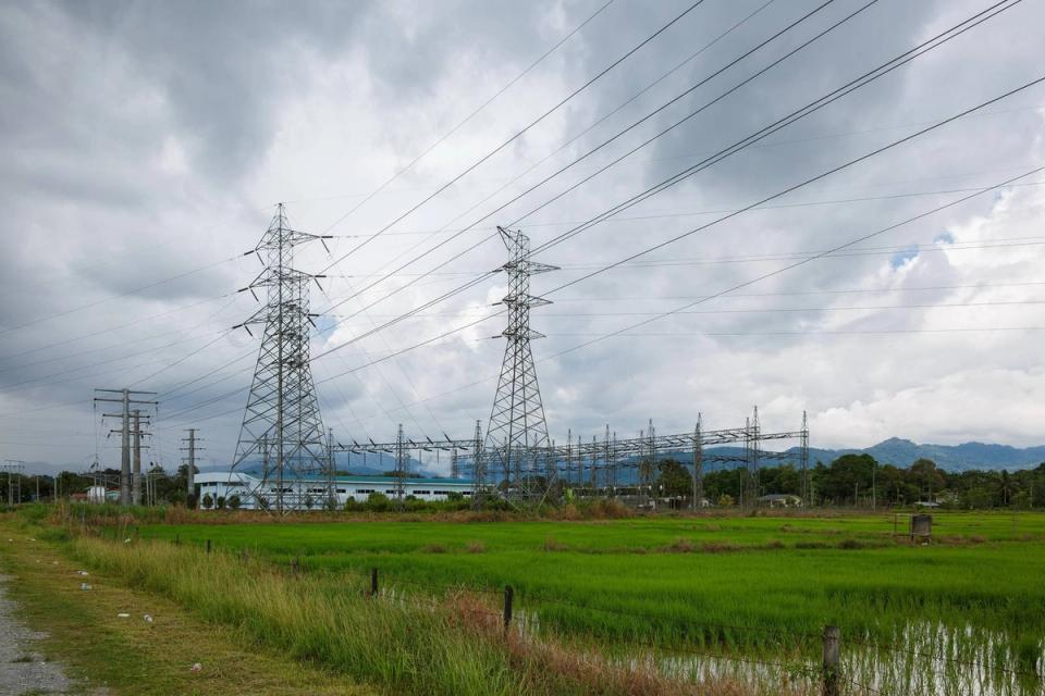 High-voltage transmission pylons and a substation beside green rice paddies under heavy clouds in Papar, Sabah, Malaysia.