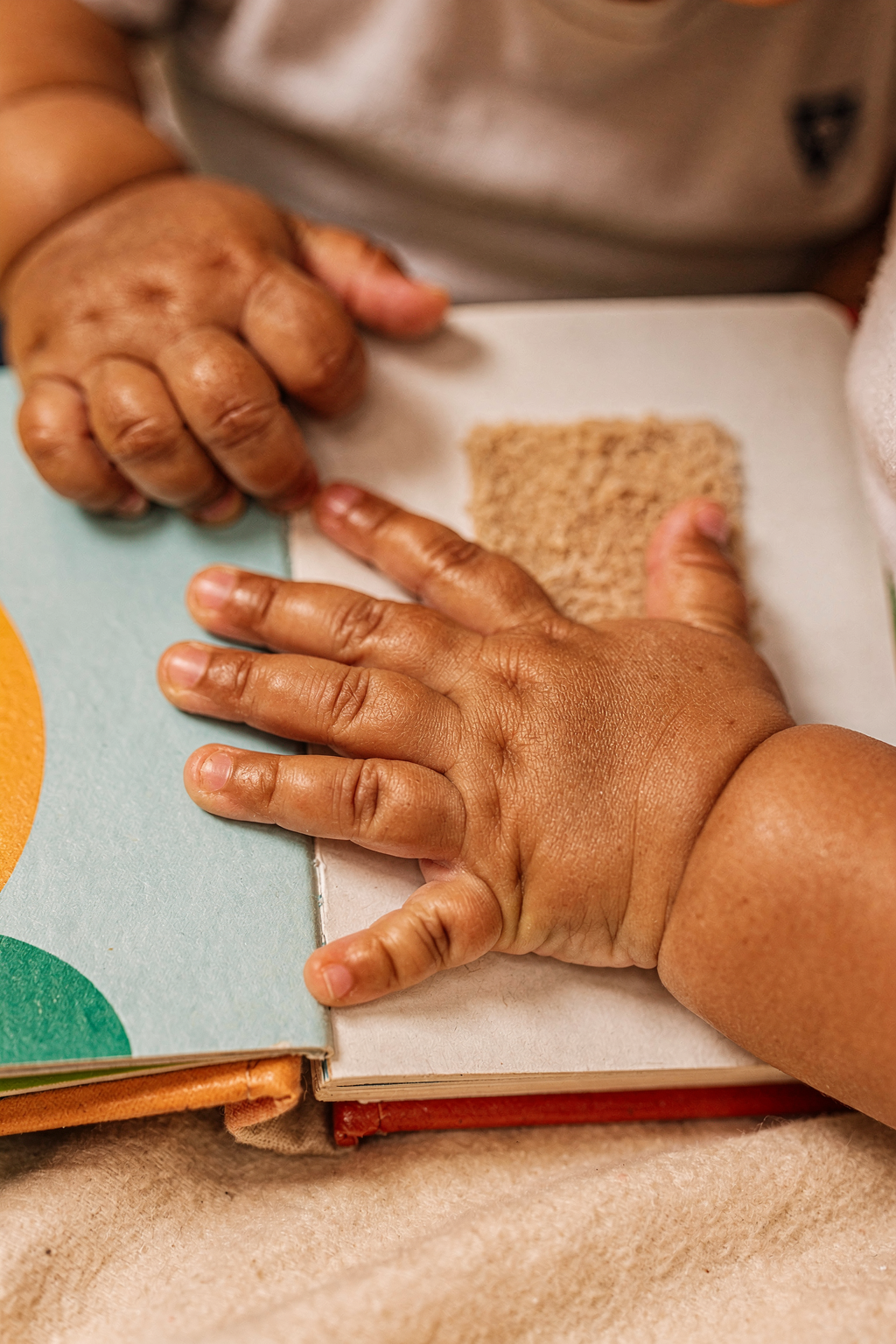 Close-up editorial photo of a baby boy's hands gripping and pressing on the textured page of an open board book, used in an article about the best board books for babies
