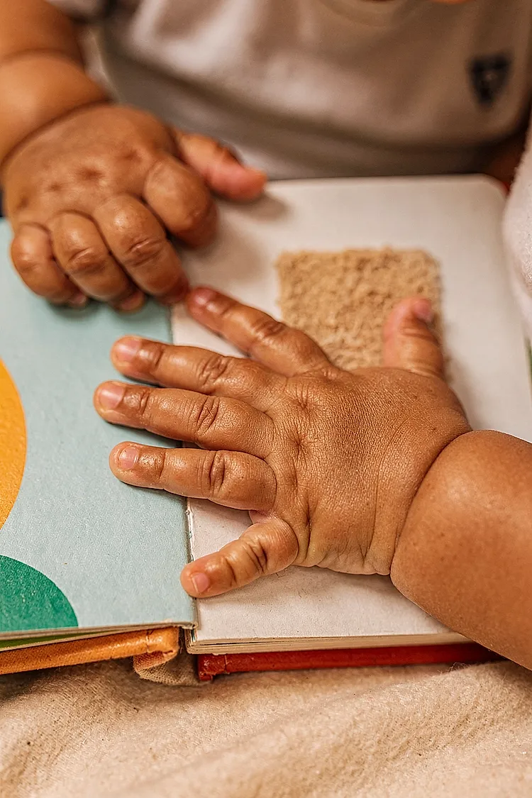 Close-up editorial photo of a baby boy's hands gripping and pressing on the textured page of an open board book, used in an article about the best board books for babies