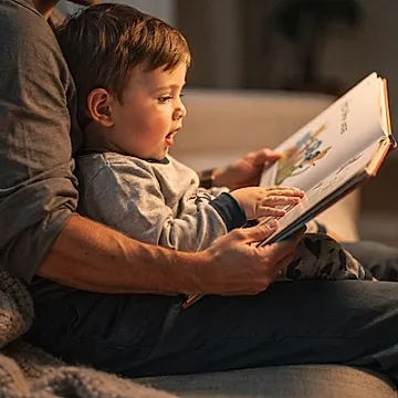 Editorial photo of a toddler boy pressing his hand against a board book page while leaning against a parent, used in an article about toddler books