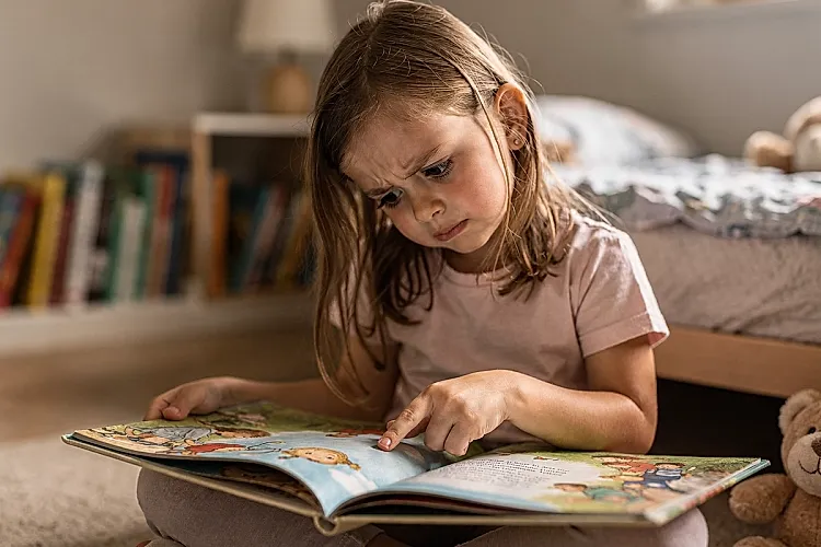 Editorial photo of a 4-year-old girl with finger on a picture book illustration and a concentrated questioning expression, used in an article about how 4-year-olds engage with bedtime stories