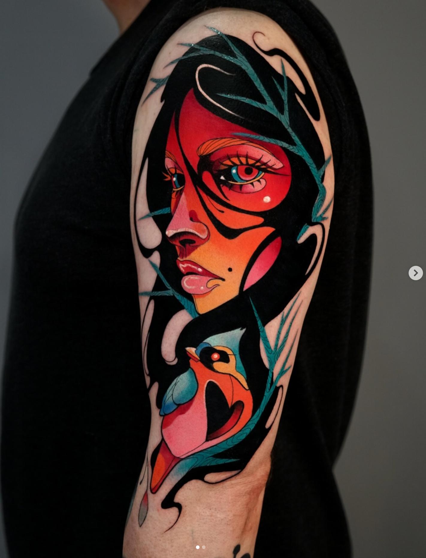 Colorful abstract face and bird tattoo on upper arm