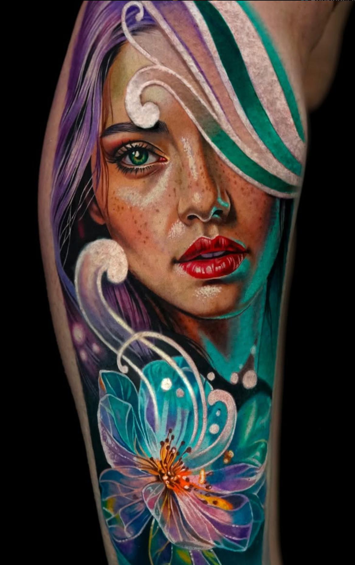 Colorful realistic portrait of a woman's face and floral design on thigh.