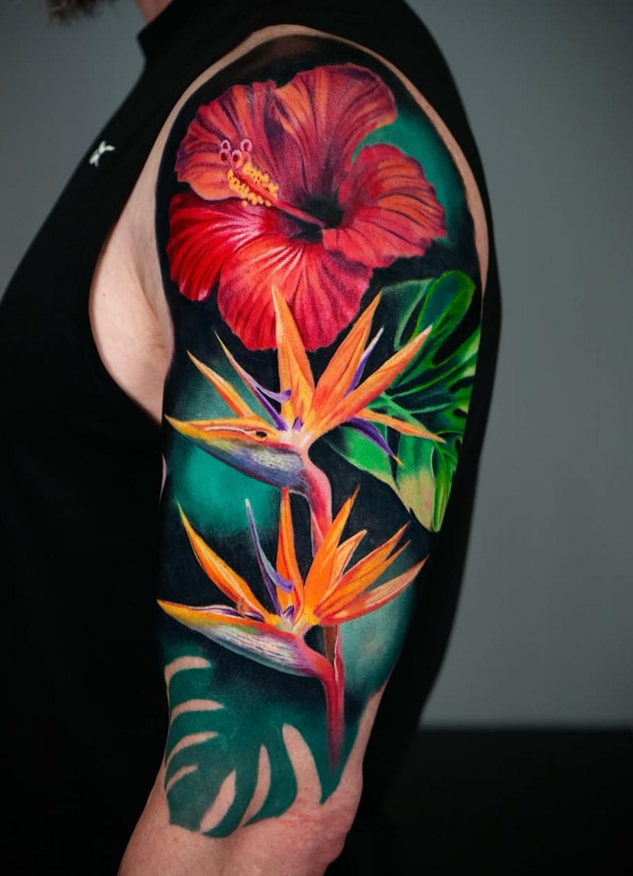 Colorful realistic floral tattoo with hibiscus and bird of paradise on upper arm