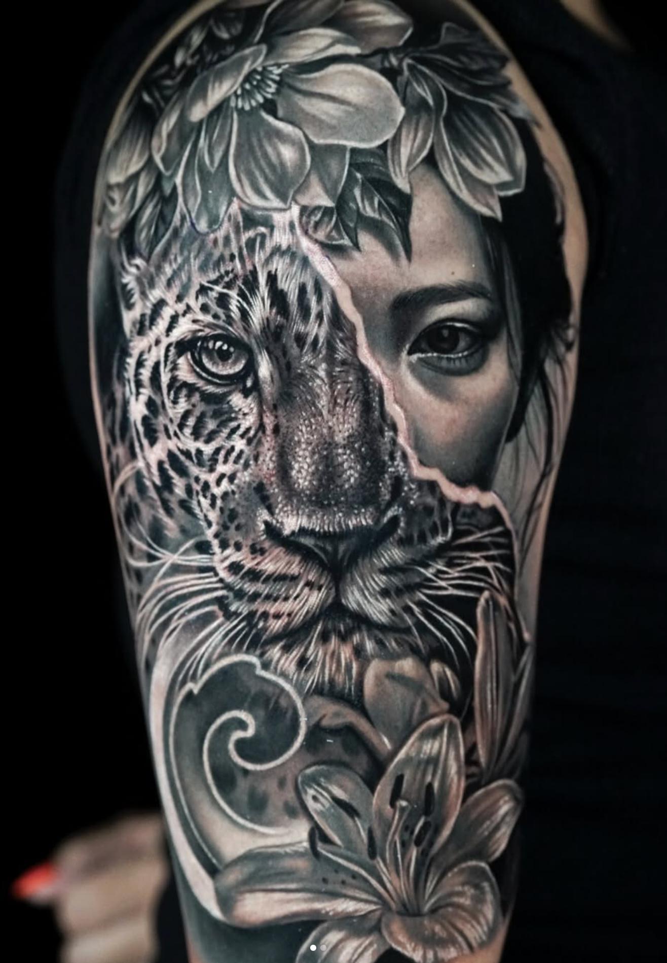 Black and grey realistic tattoo of a leopard and woman's face with flowers on upper arm