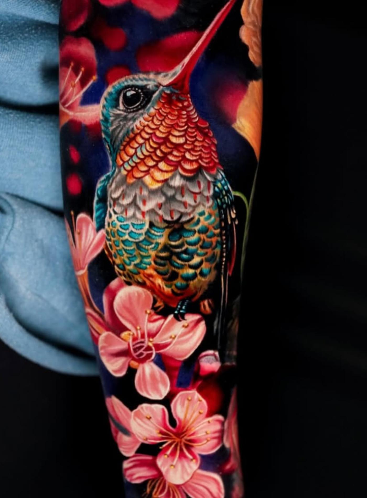 Colorful realistic hummingbird and flower tattoo on forearm