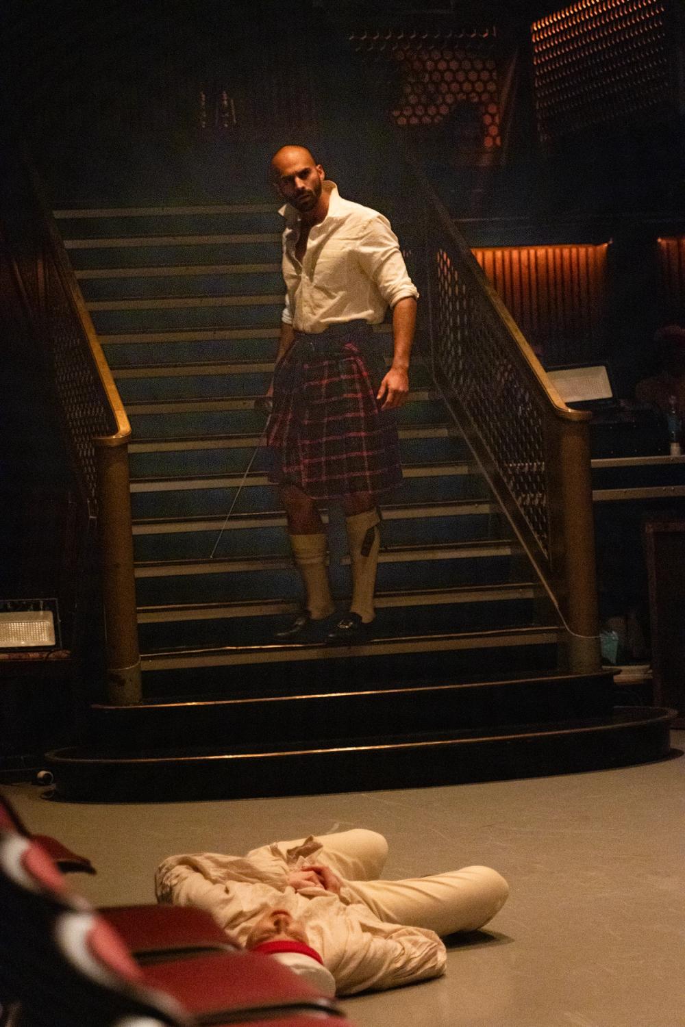 Macbeth står i trappa, med jakka av, mens en skadet matros ligger på gulvet.