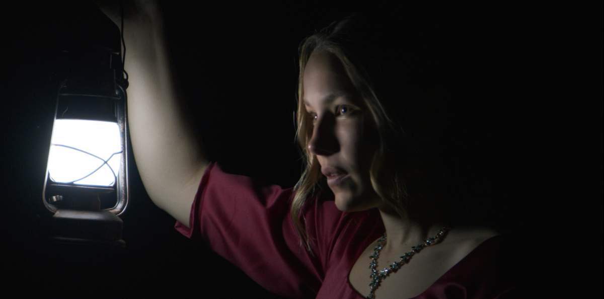 Kvinne i rød kjole som går med lykt i mørket