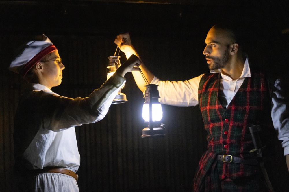 Macbeth og en matros snakker sammen, i mørket, med lykter.