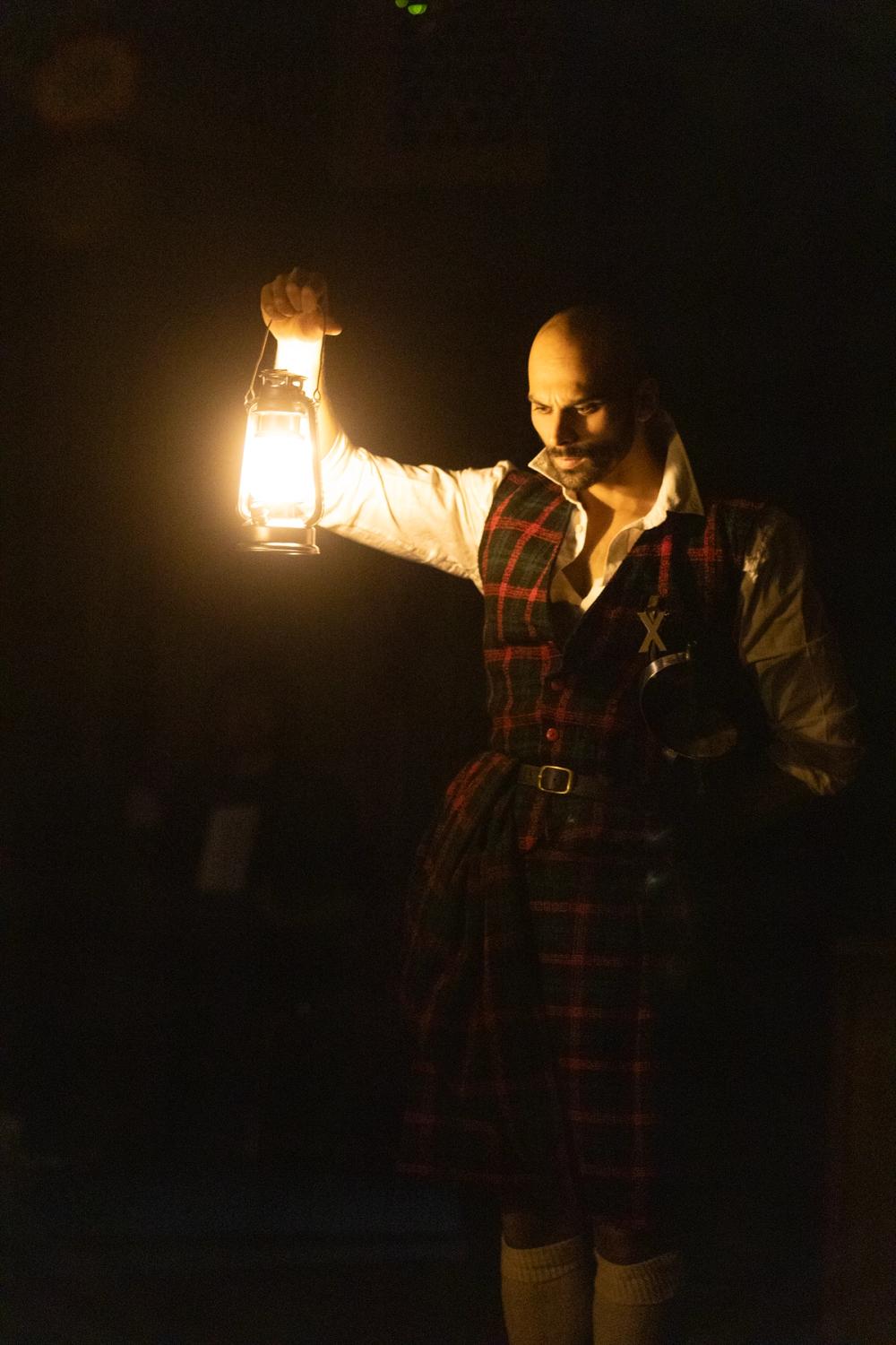 Macbeth, i kilt, står med en lykt i mørket og tenker.