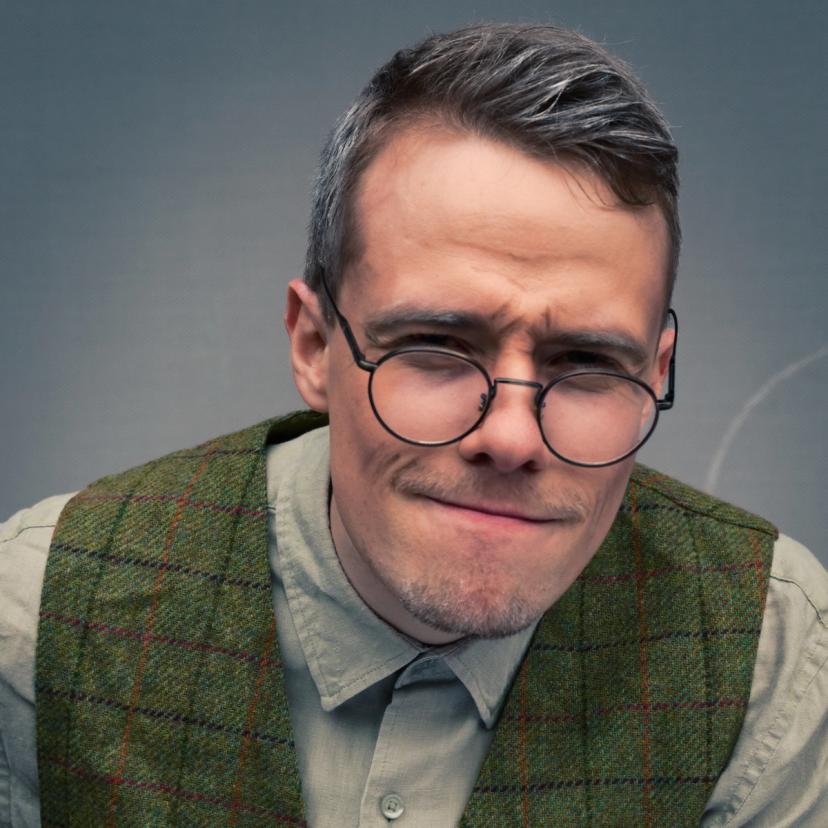 En mann med grått hår i tweedvest og briller.