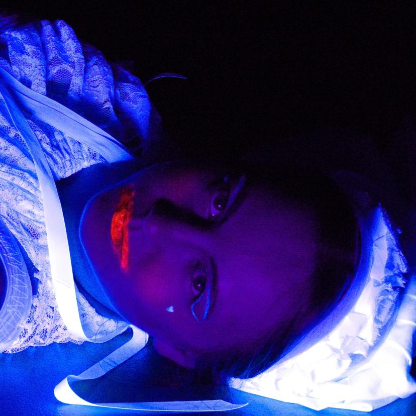 Portrettbilde av en heks som ligger på gulvet, gløder lilla og har på lysende intens leppestift.