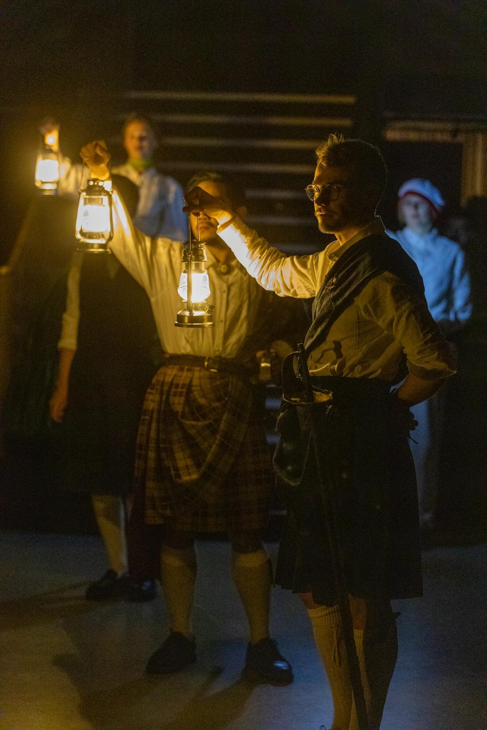 Menn i kilt med lykter i mørket.