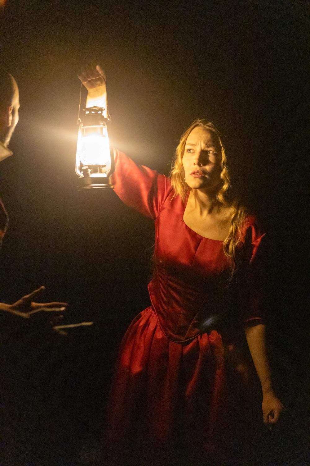 Lady Macbeth, i rød kjole, med lykt i mørket.