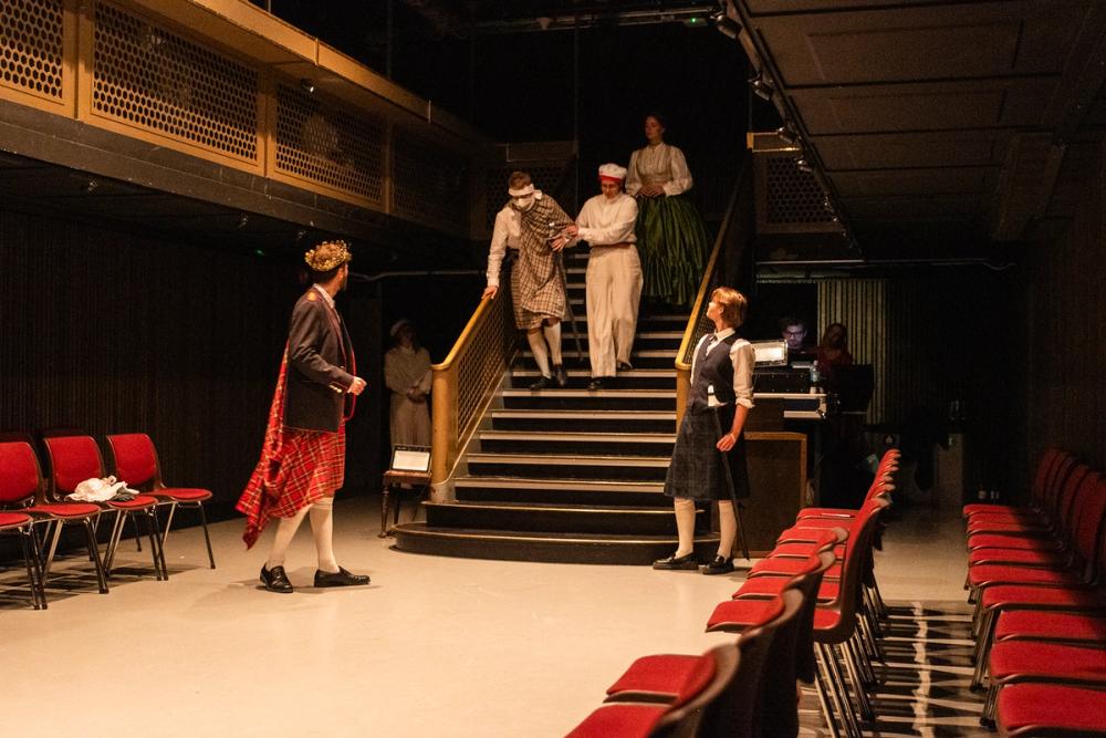 Kongen som tar imot en såret løytnant, hjulpet av en matros, på vei ned fra dekk. Prinsessen følger etter dem.