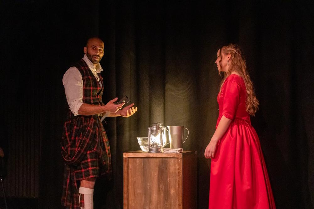Macbeth og Lady Macbeth i mørket, med en skål vann og en lykt på bordet mellom dem.