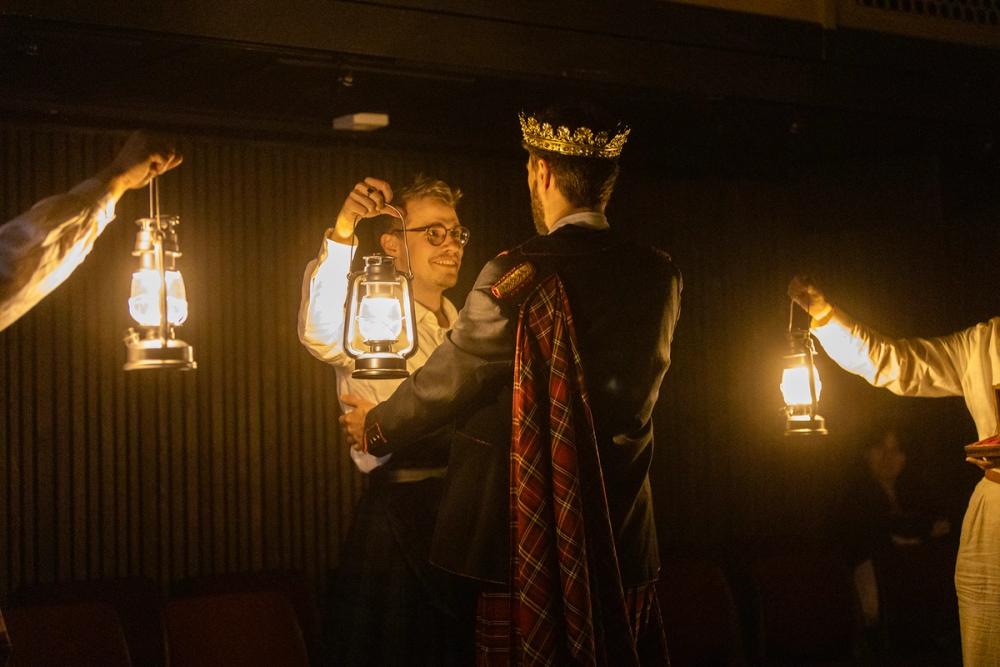 En mann som står med en lykt mens en konge i kilt snakker til ham.