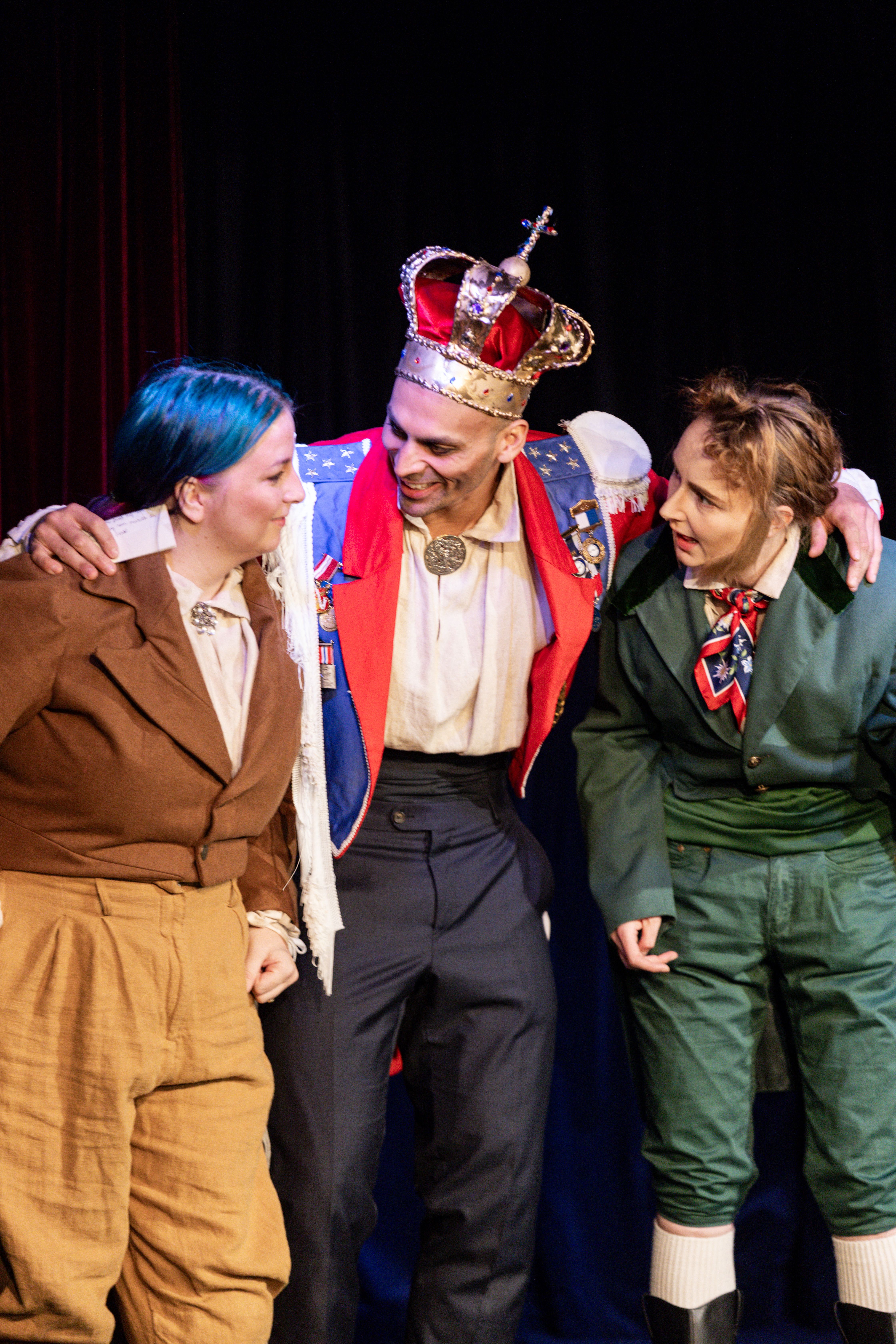 Tre skuespillere, to kledd som adelsmenn og en i midten kledd som en konge