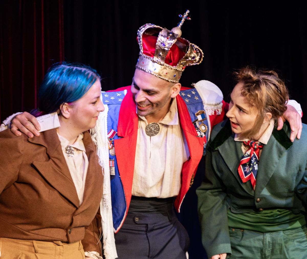 Tre skuespillere, to kledd som adelsmenn og en i midten kledd som en konge