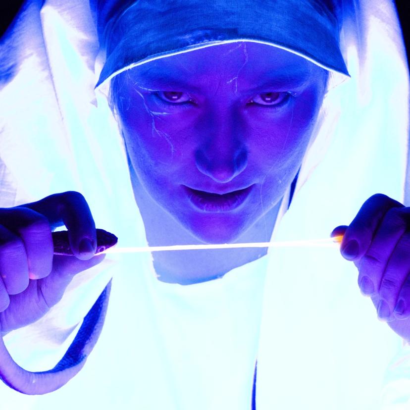 Portrettbilde av en heks som gløder, ser sløvt inn i kameraet og river tungen av en slange.