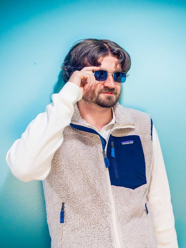 Snobbete mann med midtskill, solbriller og patagoniavest.