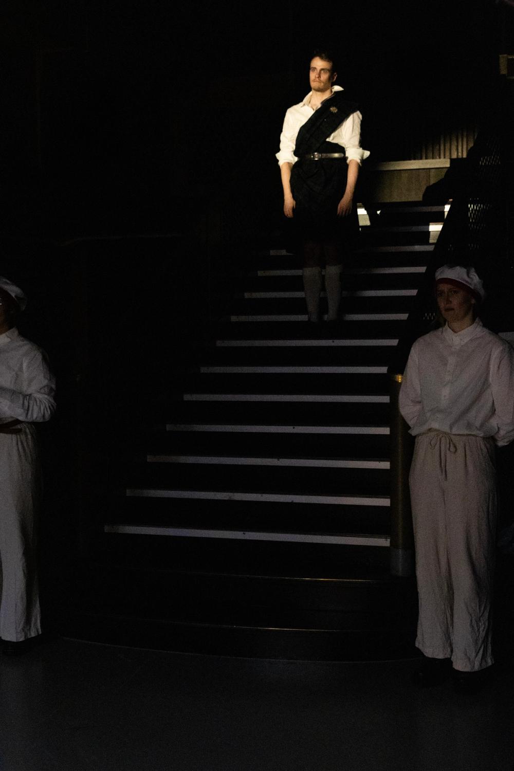 En mann står i toppen av trappa, med spotlight på seg.