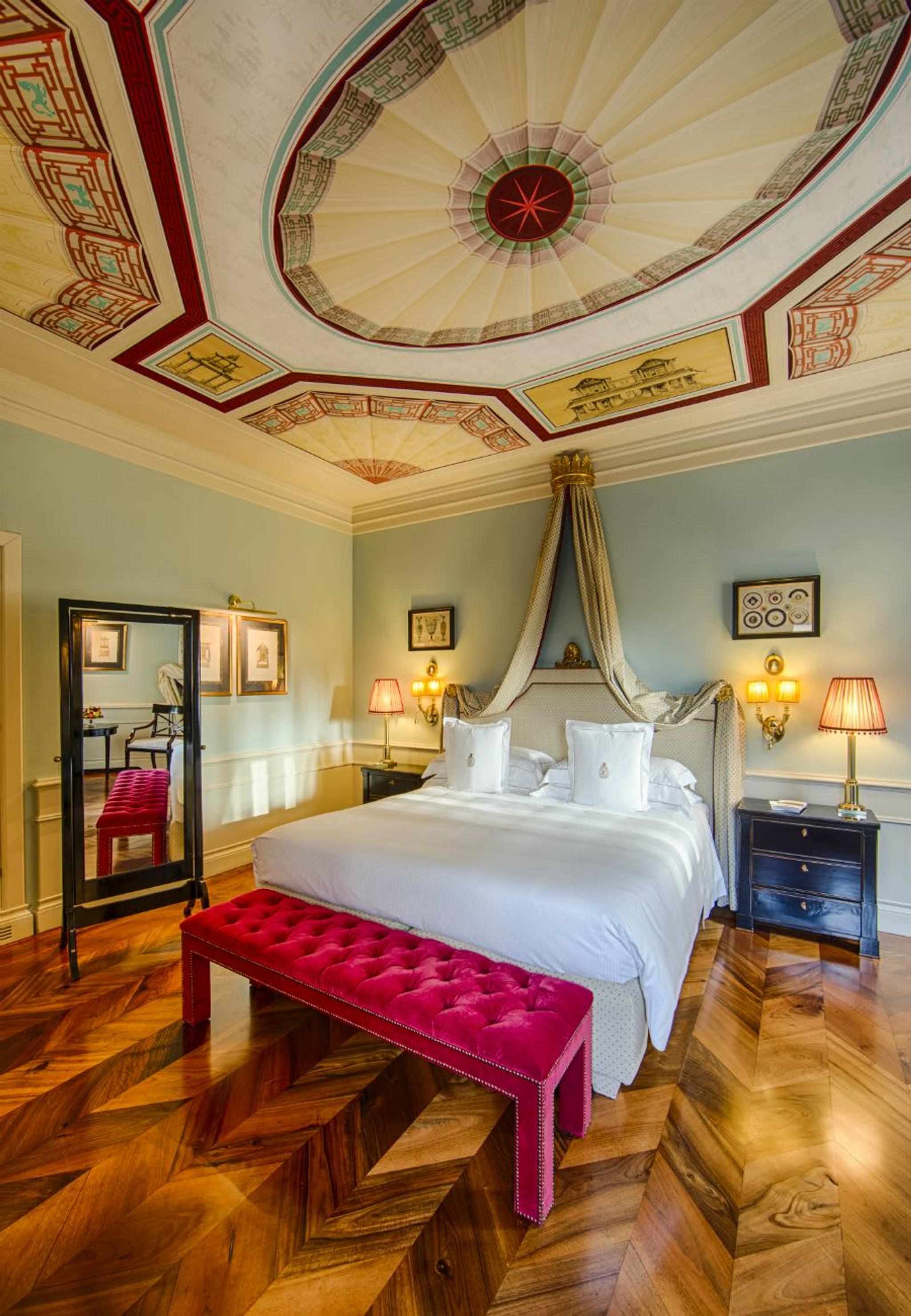Hermosos techos con frescos y un banco de terciopelo rosa brillante hacen que esta habitación Deluxe sea exquisita.