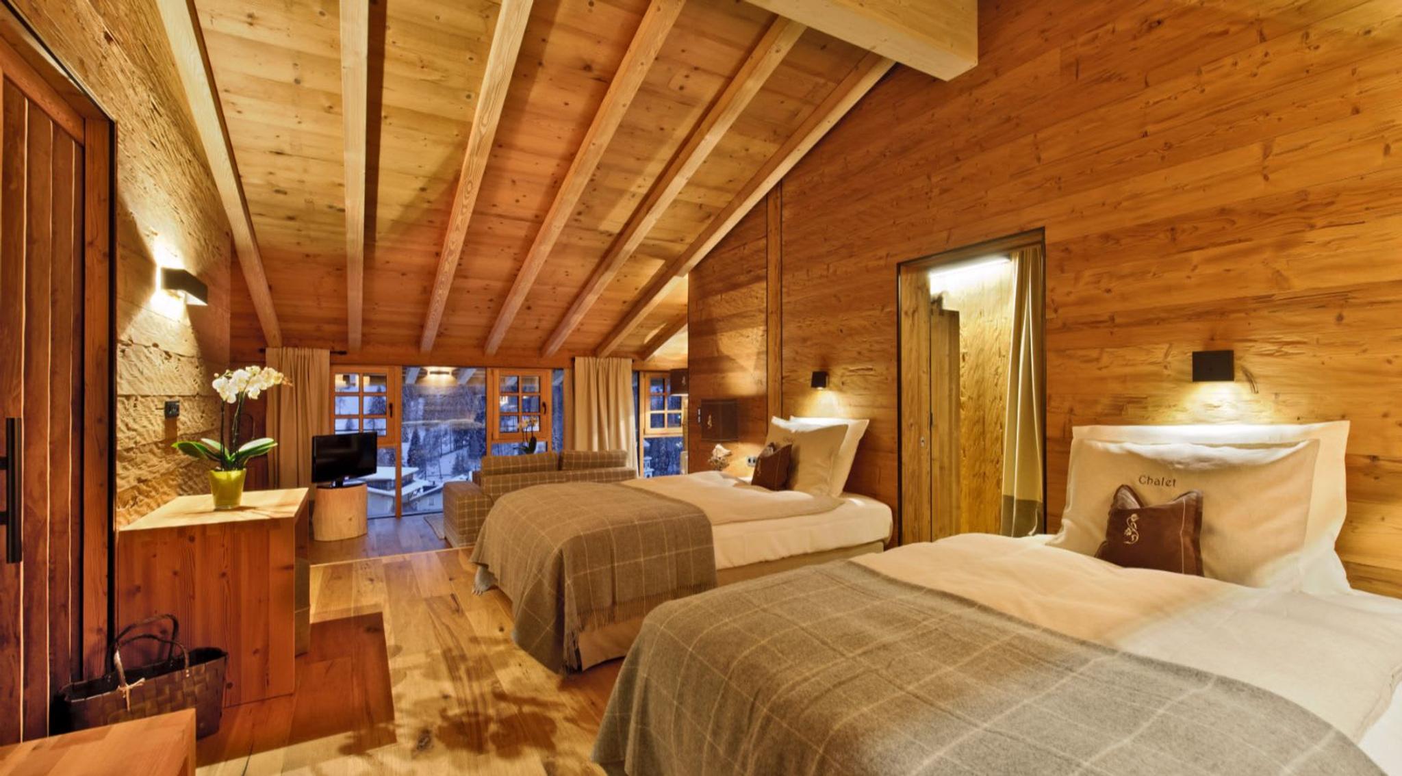 Zone de couchage du Chalet Gran Cil, l'un des cinq superbes chalets de l'hôtel Fanes, avec des intérieurs en bois, des couvertures en tartan de cachemire et une vue panoramique à couper le souffle sur le village et les pistes.