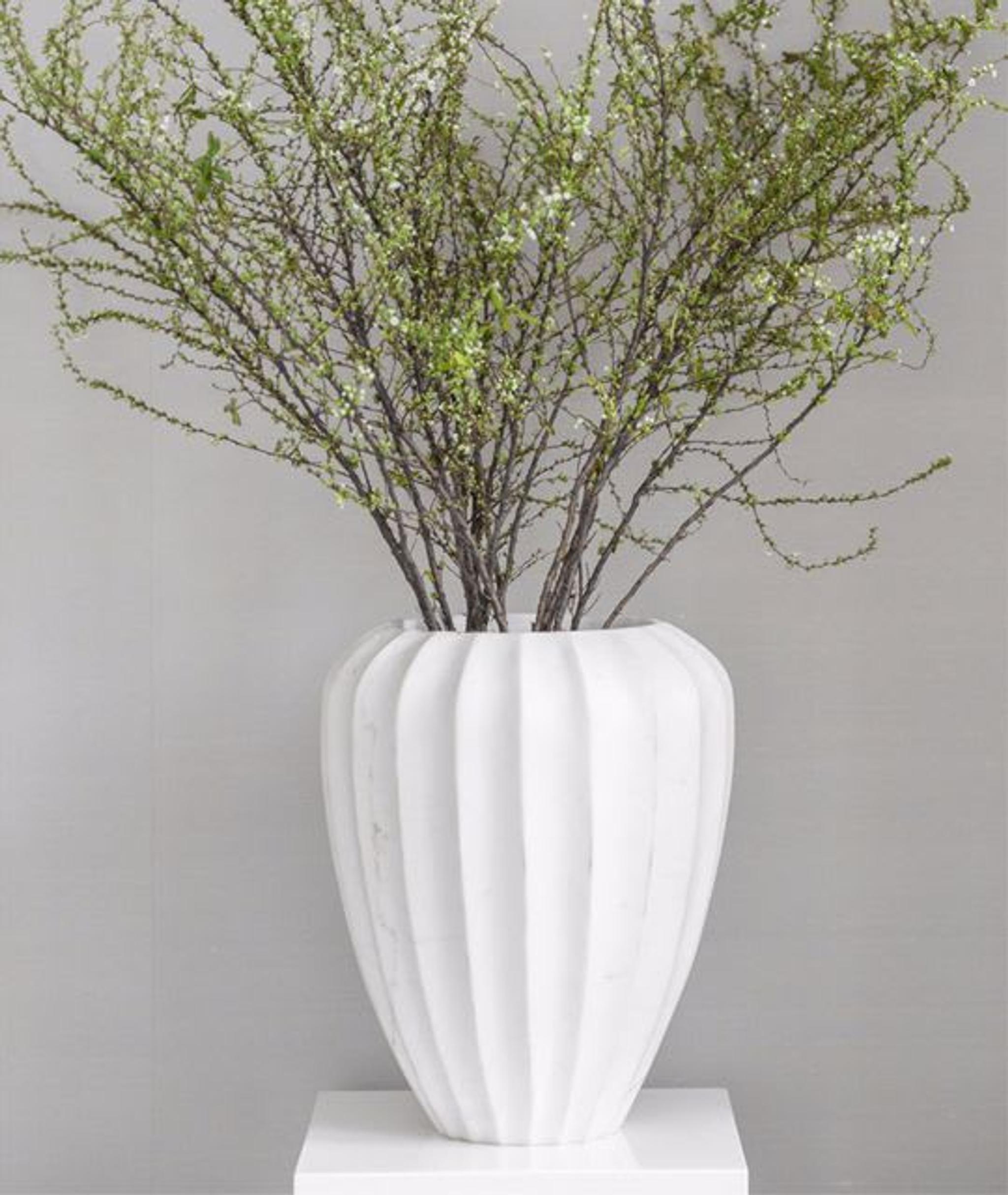 Raffinierte Dekorationsdetails - eine Keramikvase mit langen grünen Zweigen der Saison verleiht einen Hauch von Grün