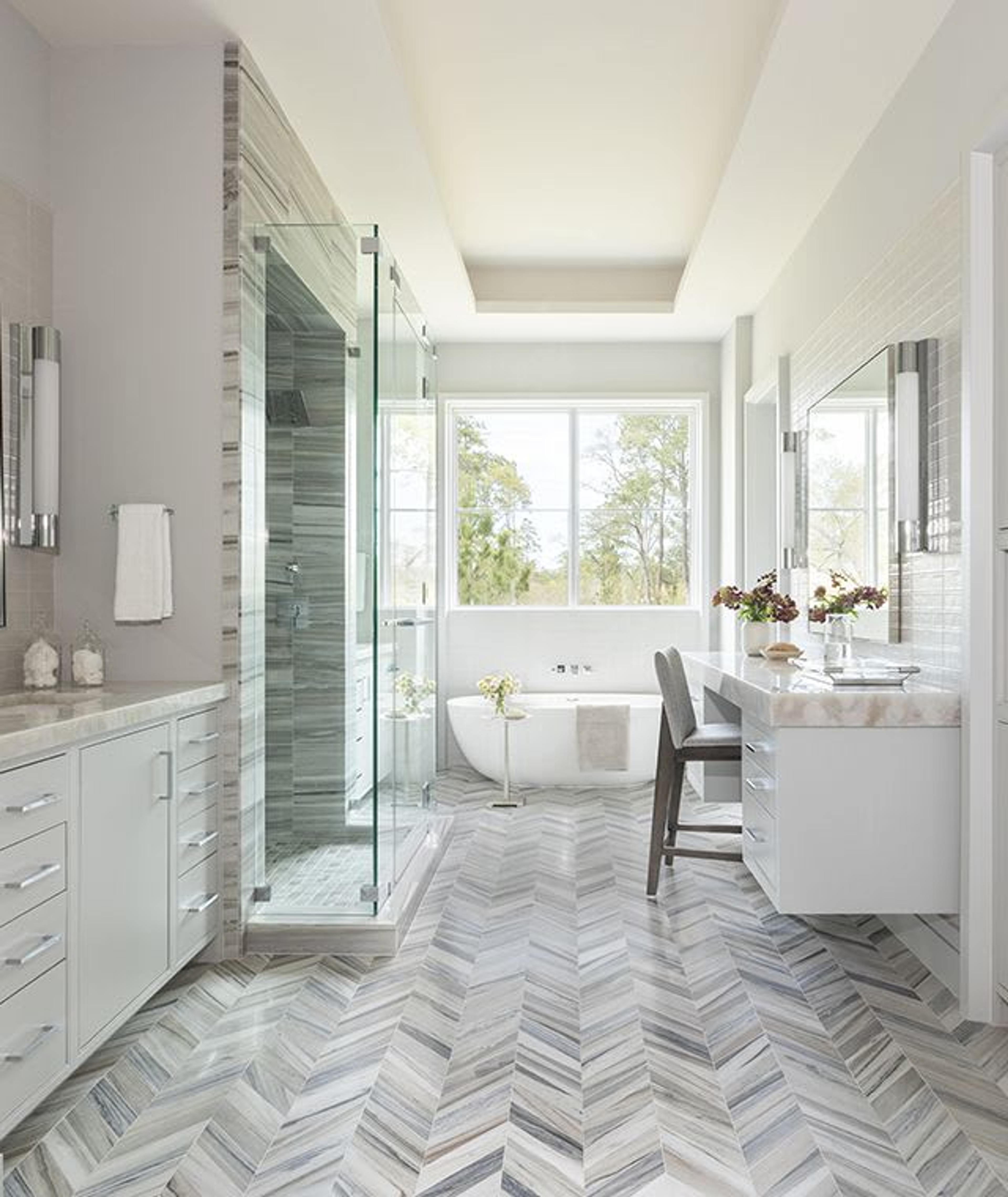 Un suelo de mármol en espiga juega con el contraste y proporciona una pasarela hacia los tocadores dobles y la bañera de hidromasaje en este baño principal inspirado en un spa.