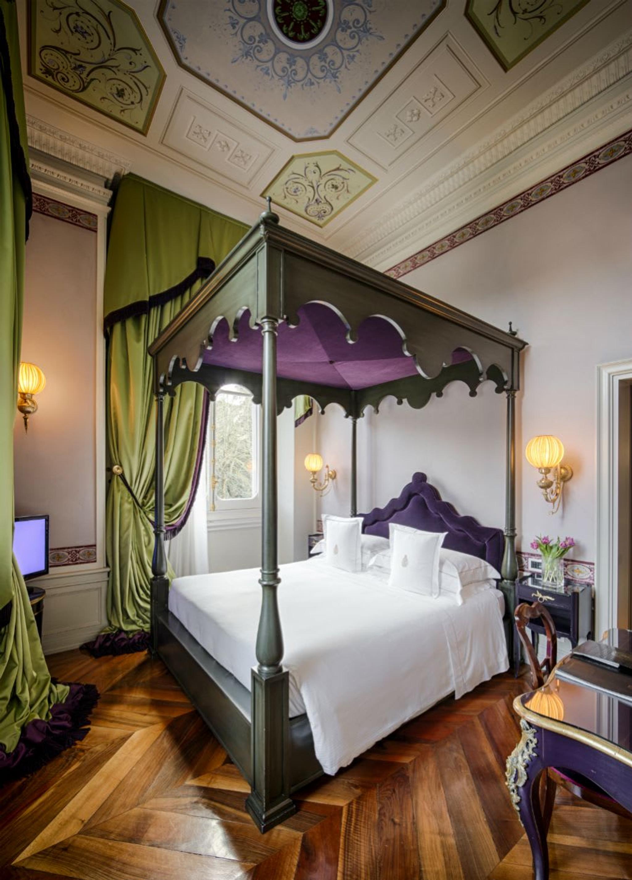 Vista de una elegante suite en tonos verdes y morados con una regia cama con dosel y preciosos frescos.