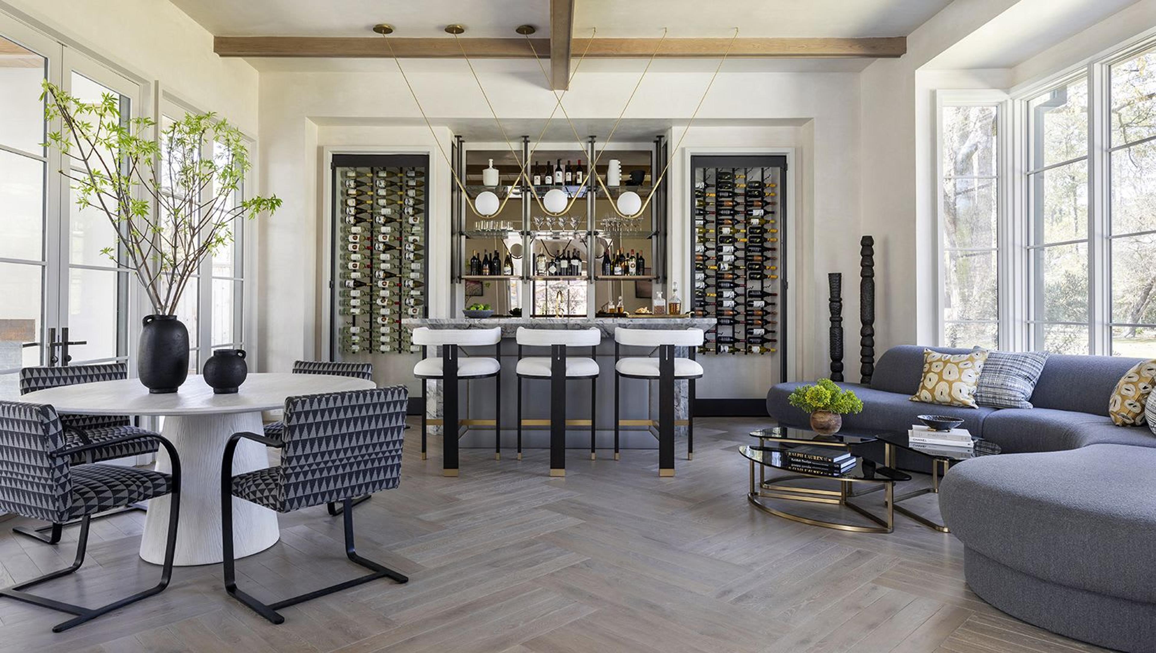 Designed for entertaining, this bar and lounge features dual wine coolers, open shelving, and an aged brass trio pendant featuring hand-blown glass. The bar surface features a unique waterfall stone profile with a thick mitred edge and a reverse bevel that conceals enclosed LED lighting. Curvilinear furnishings and a game table rest atop compound herringbone floors creating the ideal place to spend quality time with friends and family.