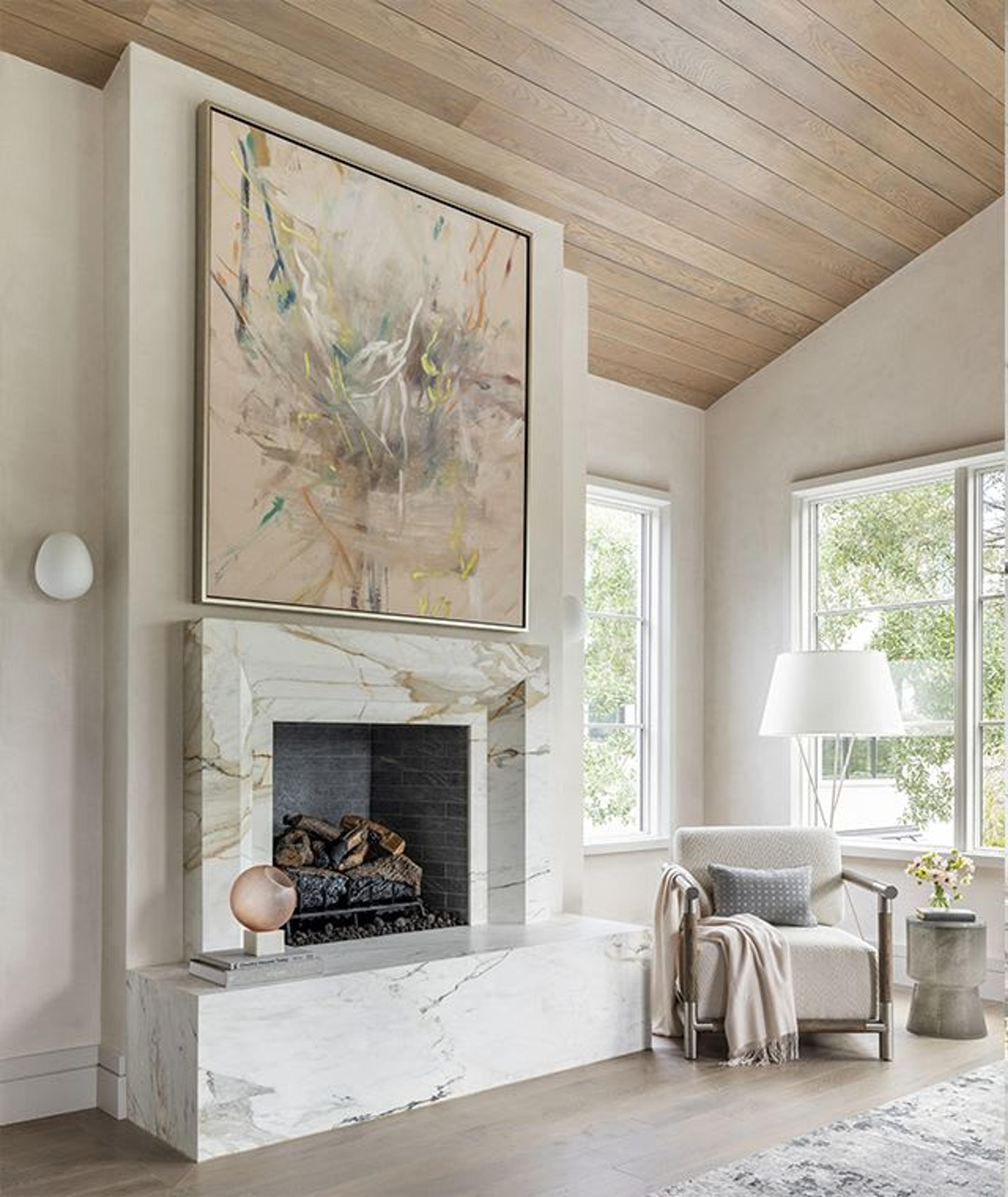 The vaulted wood ceiling in this primary retreat gives way to plaster walls that frame a massive fireplace custom-designed to lend drama and dimension. An abstract art piece provides visual cues that inspire the surrounding decor.
