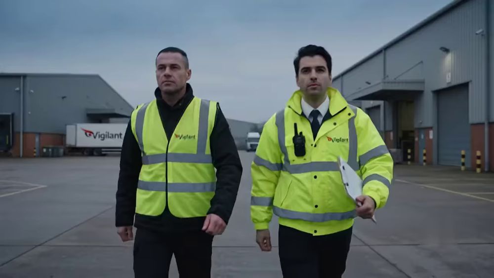 Two security officers in high-visibility jackets patrolling a yard
