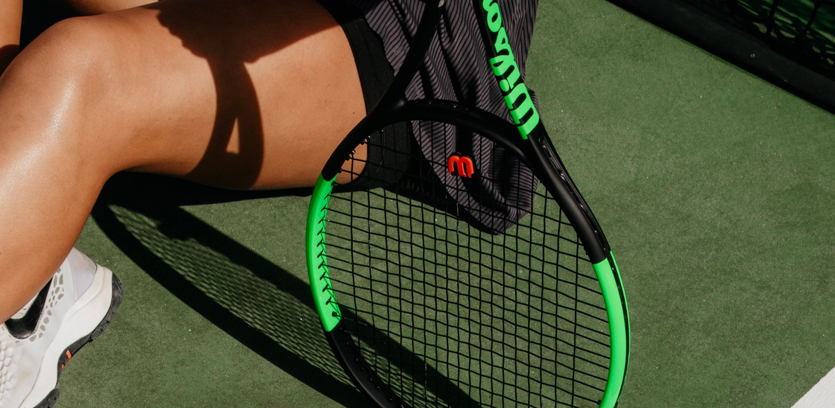 Three yellow Wilson US Open tennis balls rest on a black and blue tennis racket, all on a blue textured surface.