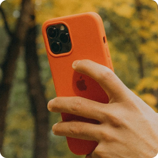 A person holds a smartphone with a dark green case, showing their hands with light nail polish.
