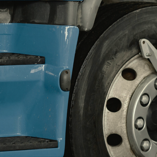 Close-up of a blue truck's side with a black step, small marker light, and tire.