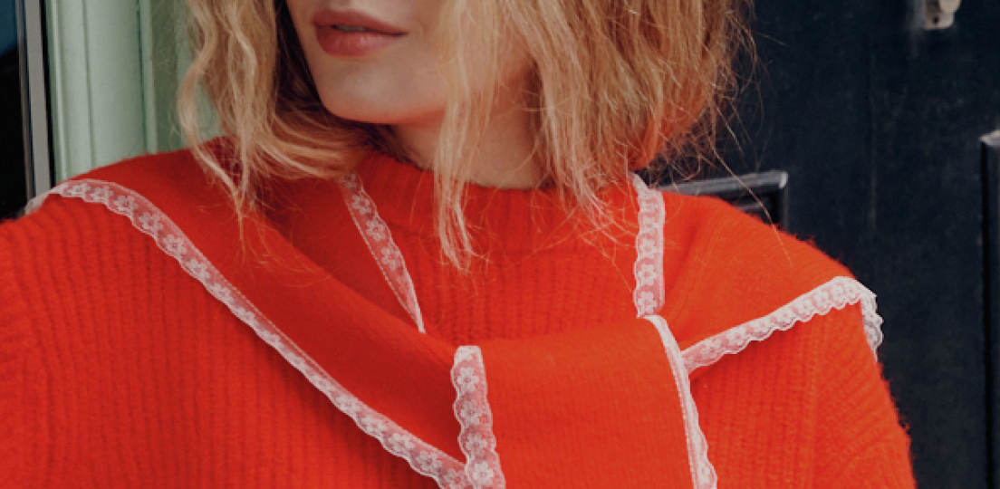 Close-up of a woman in an orange ribbed sweater with a matching scarf trimmed in white lace.