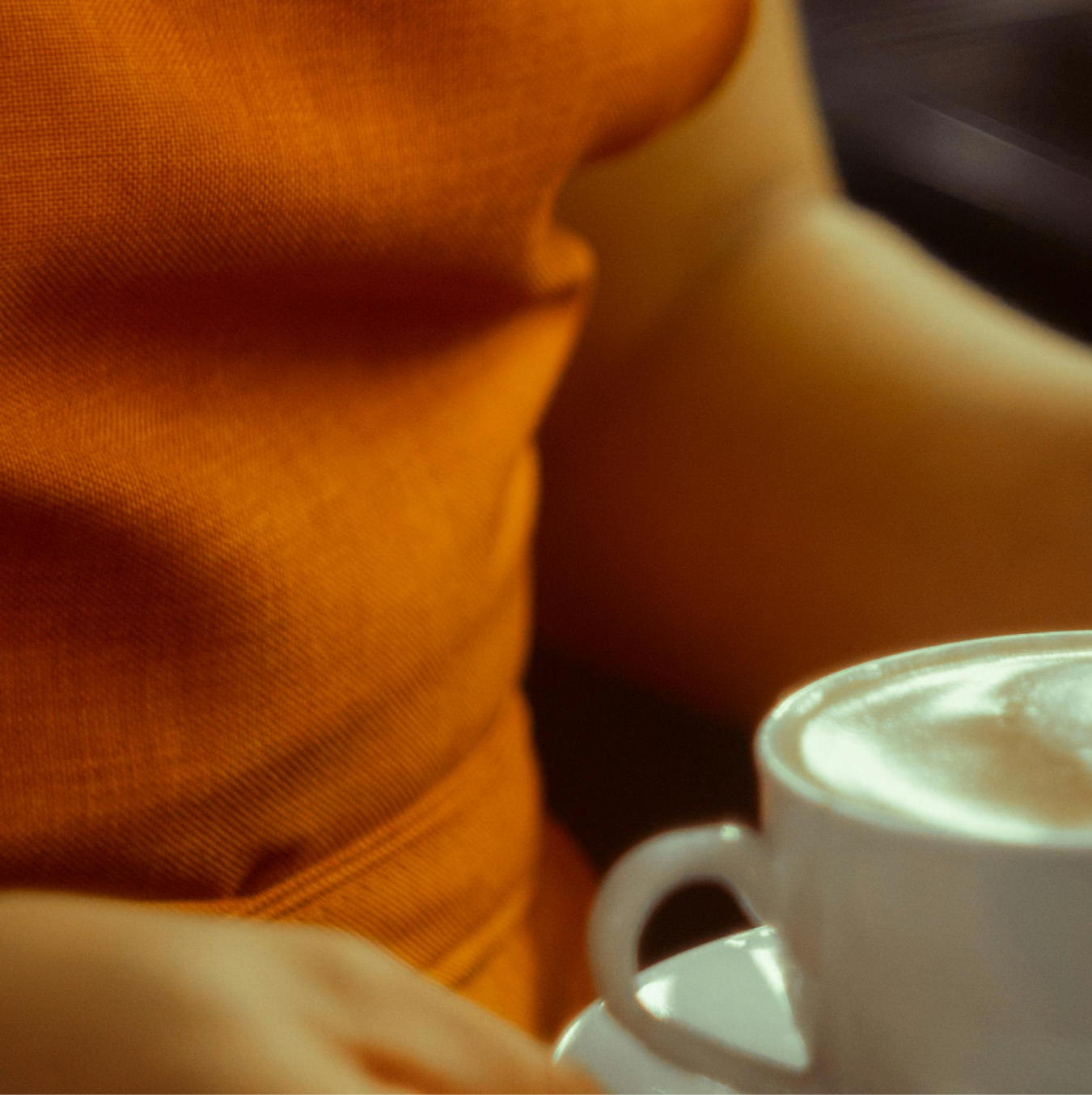 A person in an orange shirt with a white cup of foamy coffee.