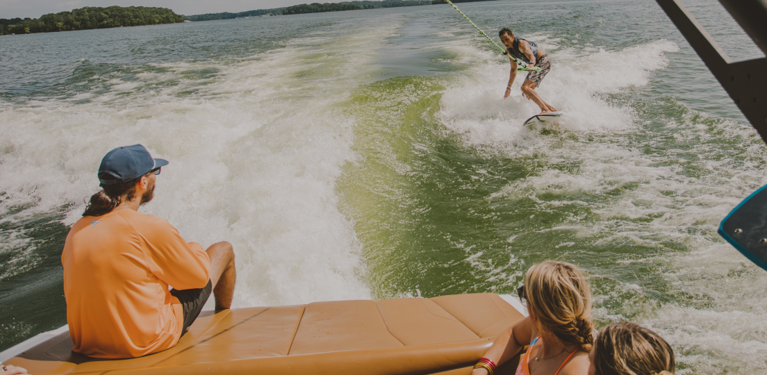 A man wakesurfing behind a boat, watched by three women.