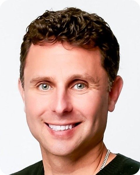 Headshot of a smiling man with curly brown hair and light eyes.