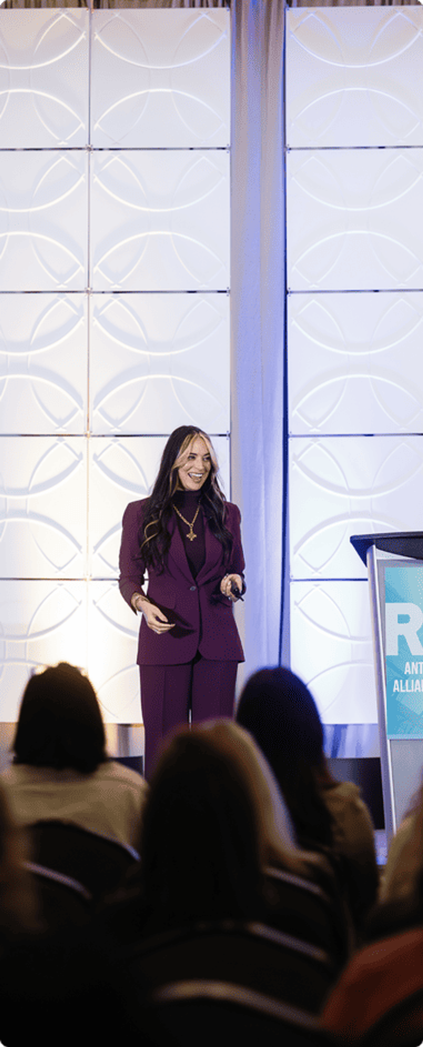 A speaker in a plum suit smiles while addressing the ATAC audience from the stage.