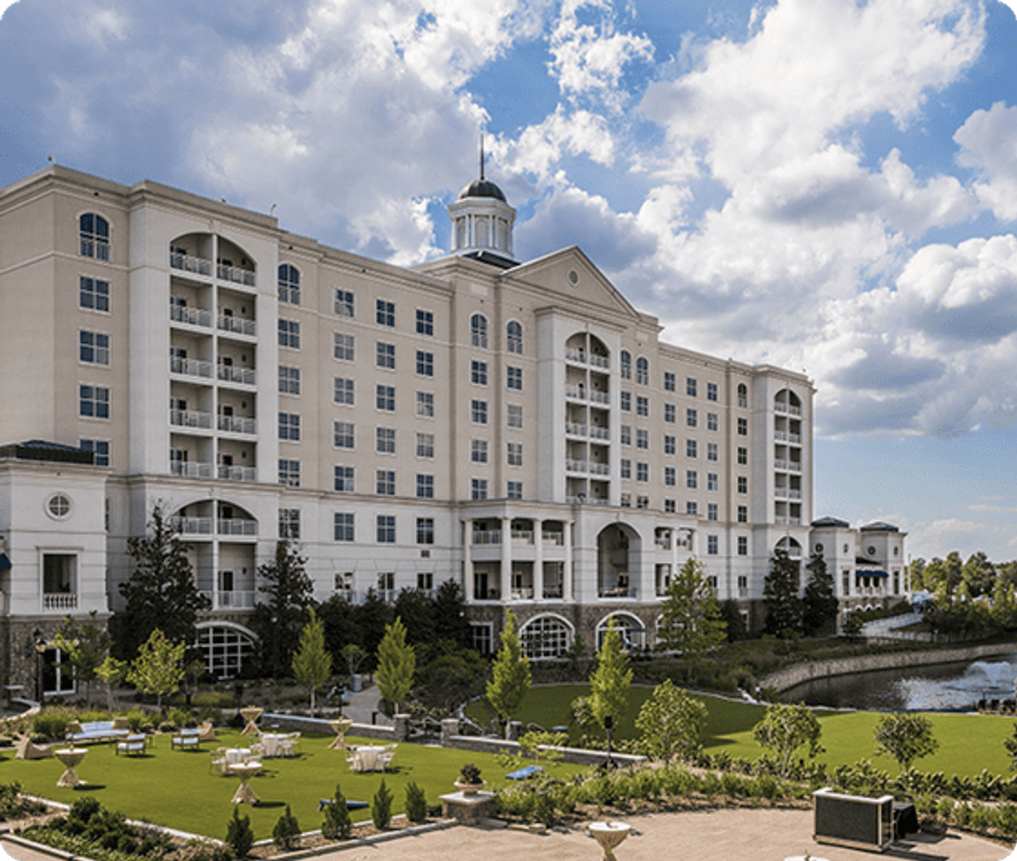 Exterior of The Ballantyne Hotel in Charlotte, a cream multi-story building with a cupola above a manicured lawn and gardens.