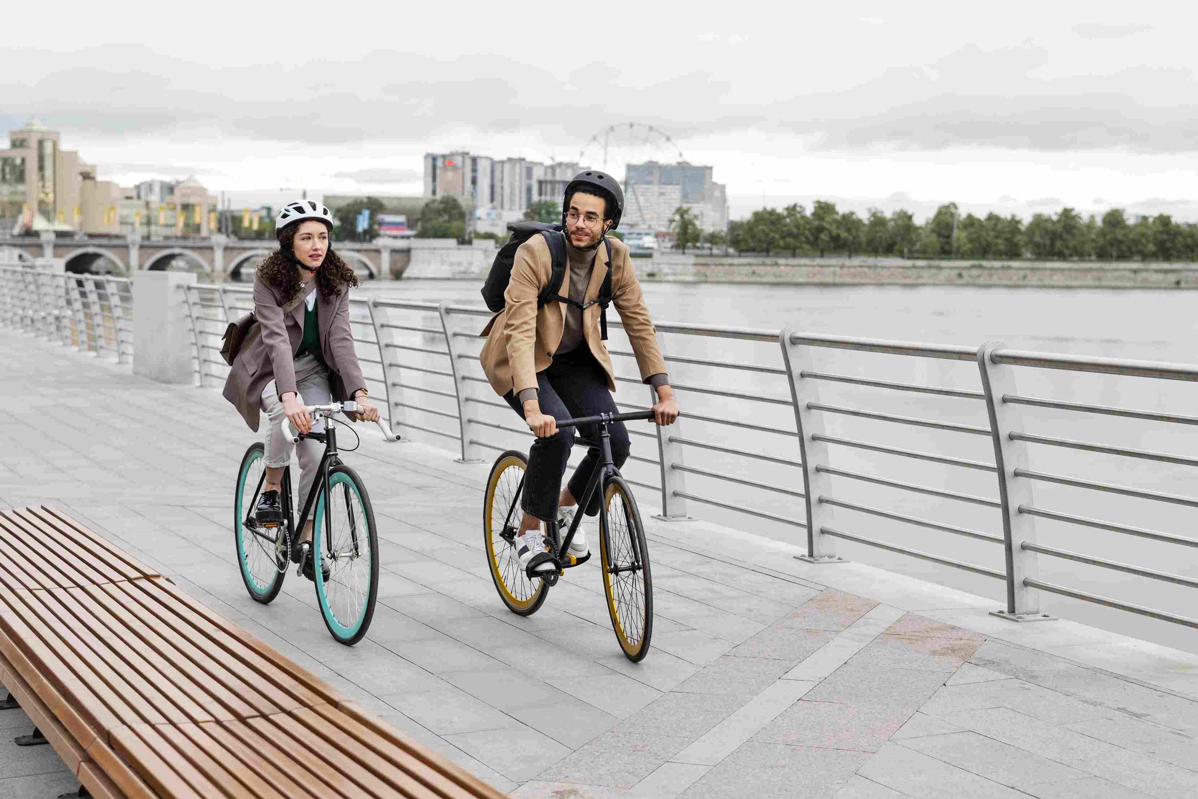 Two cyclists wearing helmets navigating a scenic riverside path on e-bikes.