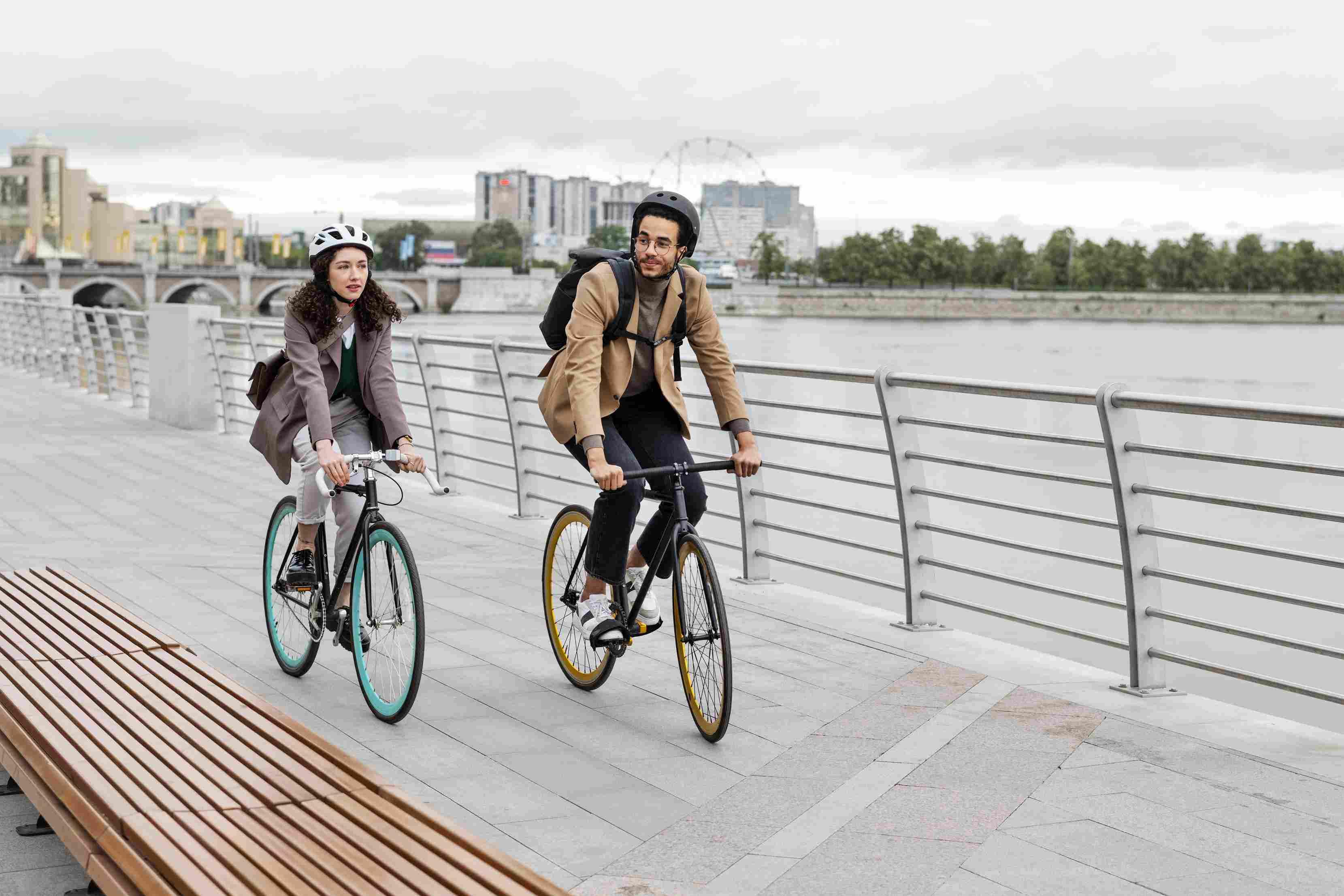 Two cyclists wearing helmets navigating a scenic riverside path on e-bikes.