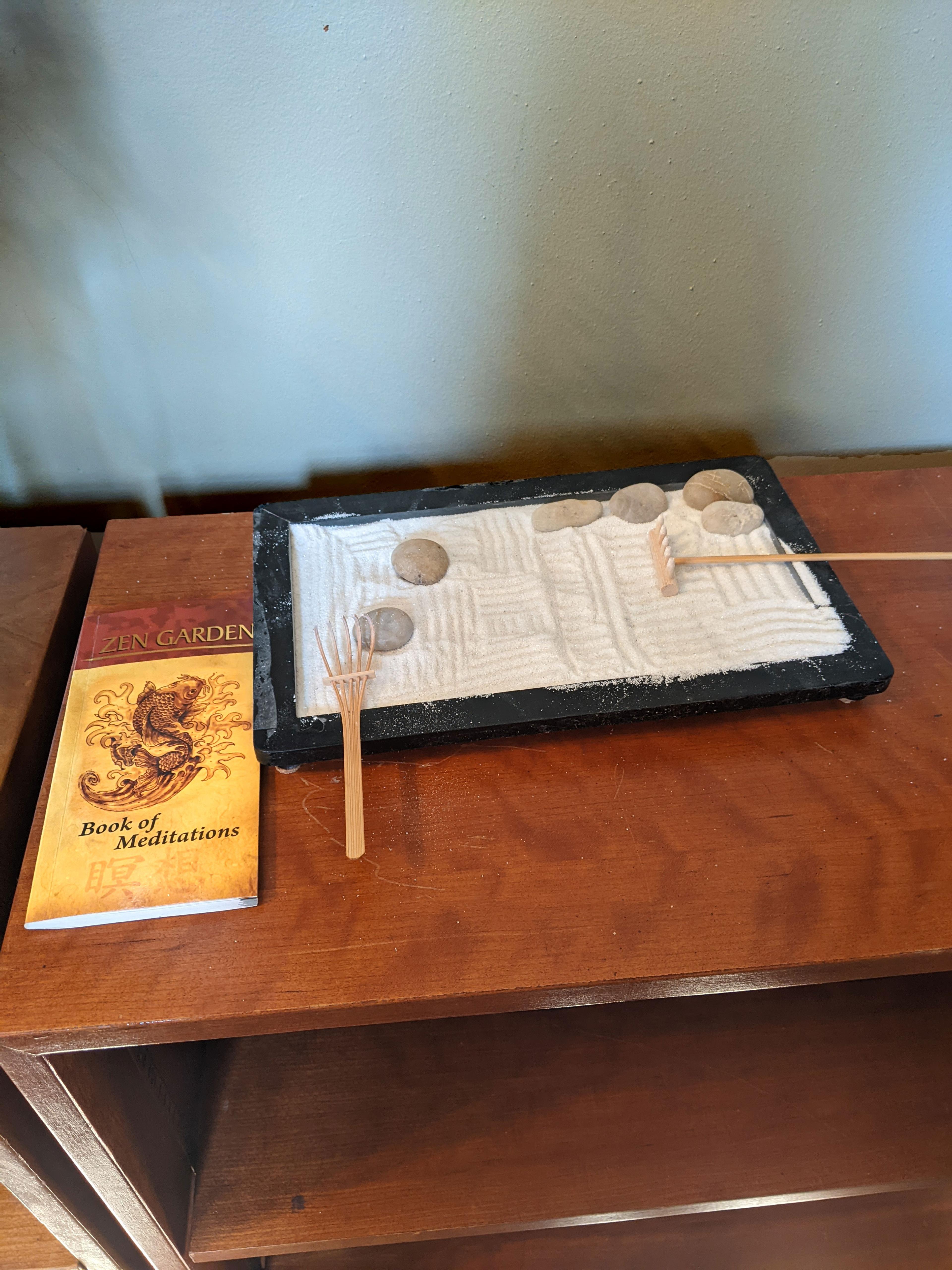 A miniature zen garden set up right behind the podium with a book on meditation beside it