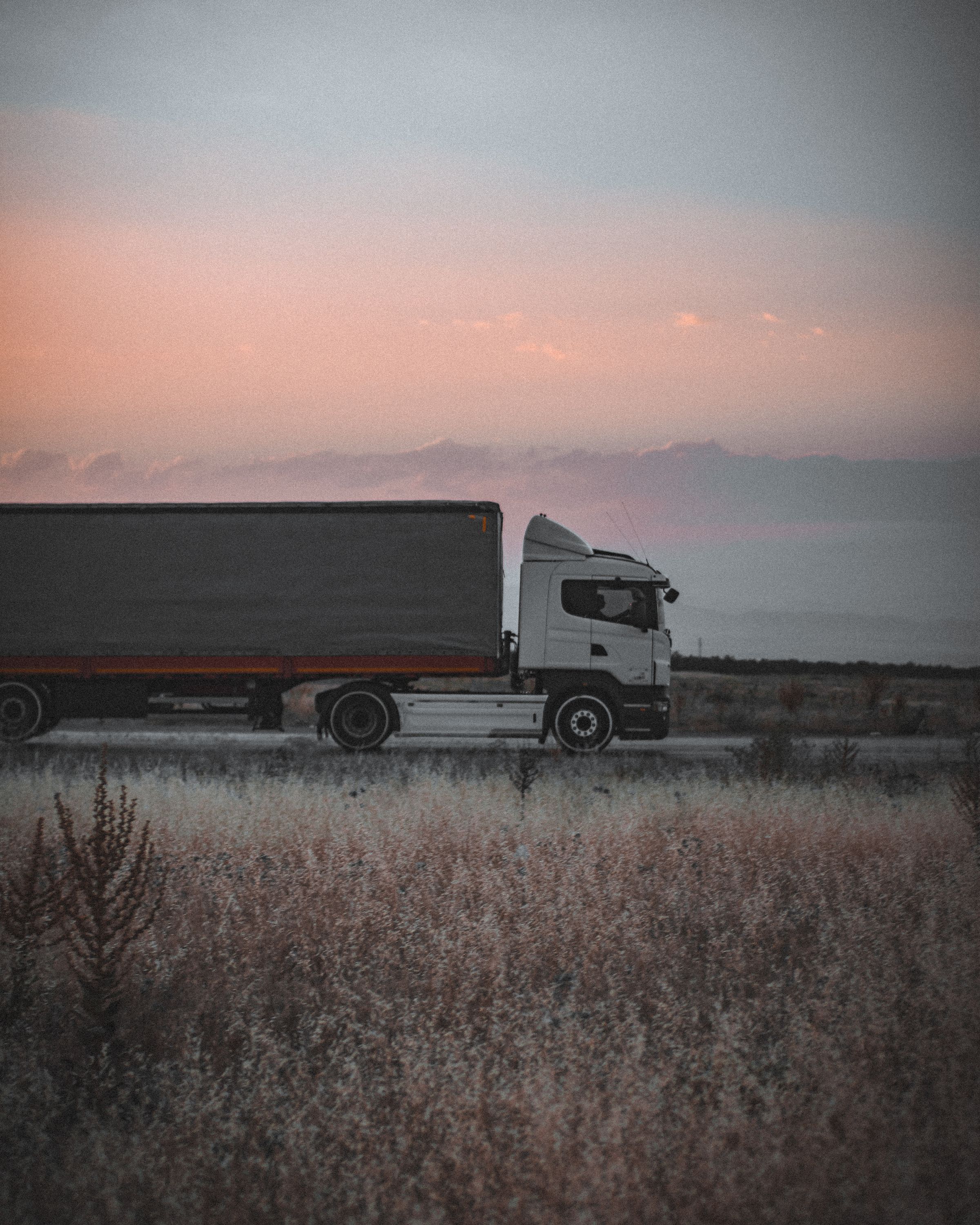 Camion semi-remorque bâché sur une route au coucher du soleil