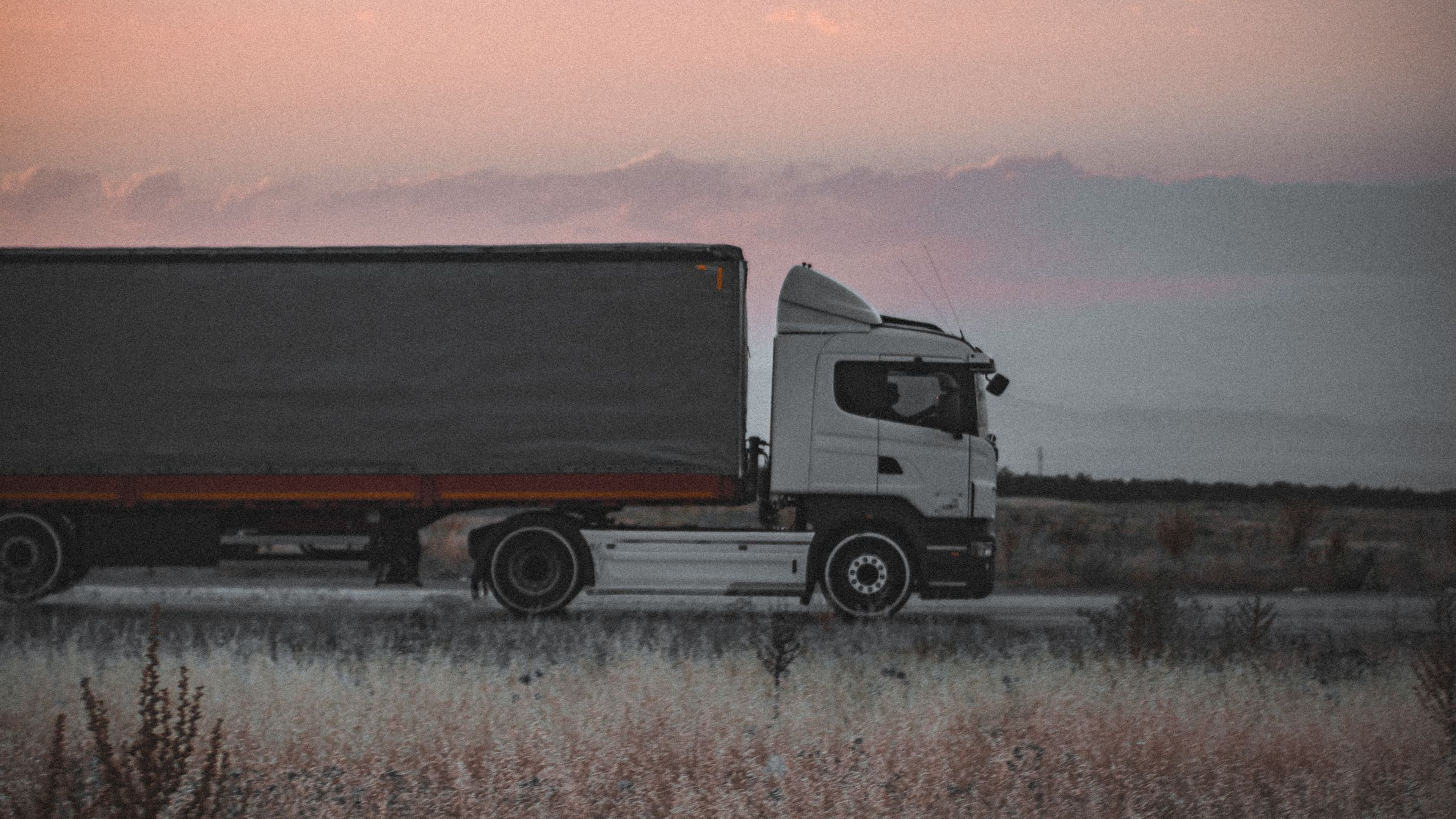 Camión con semirremolque de lona circulando por carretera al atardecer