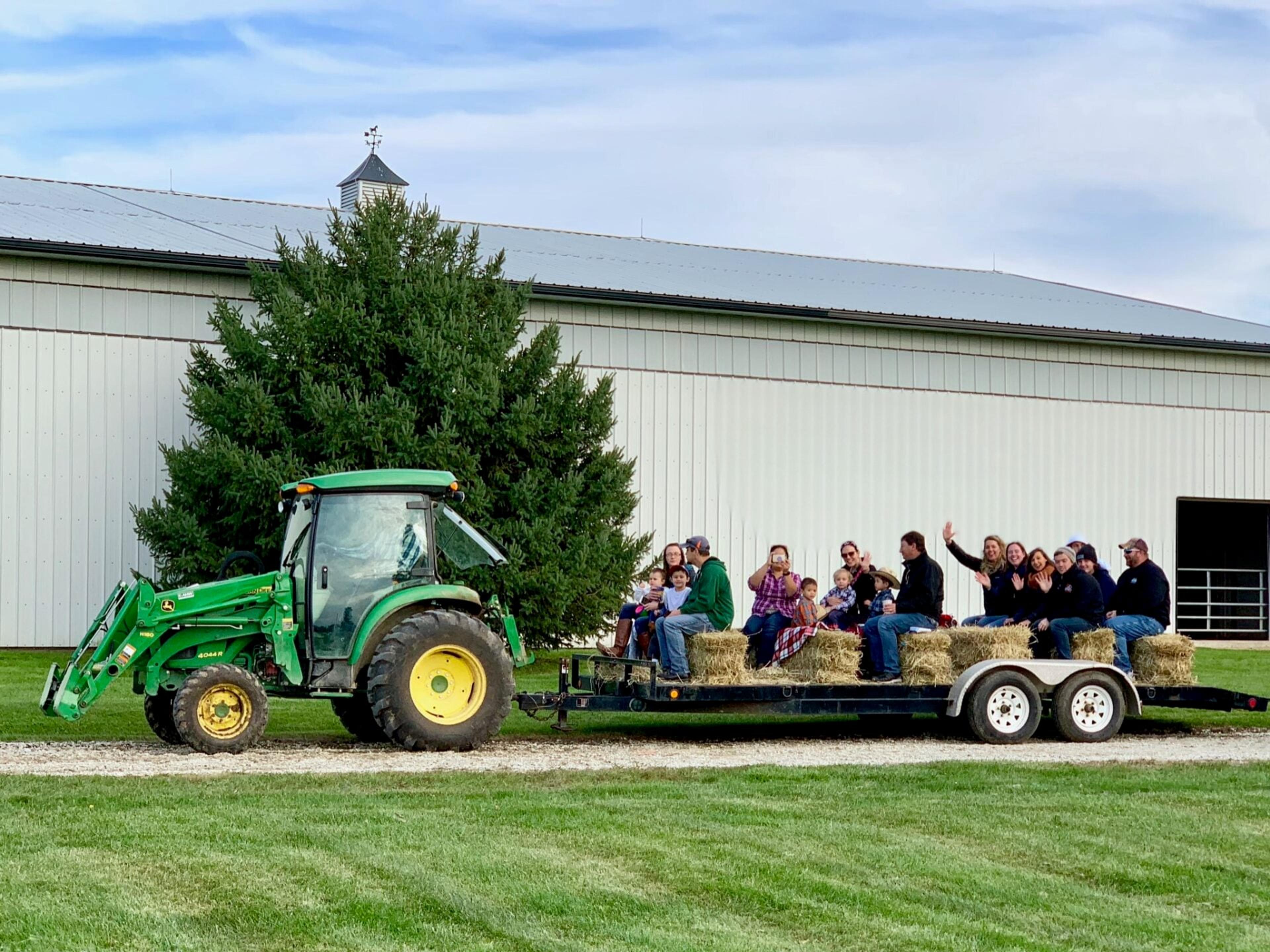 Staff ride a tractor-pulled hay wagon past a white barn on staff appreciation day