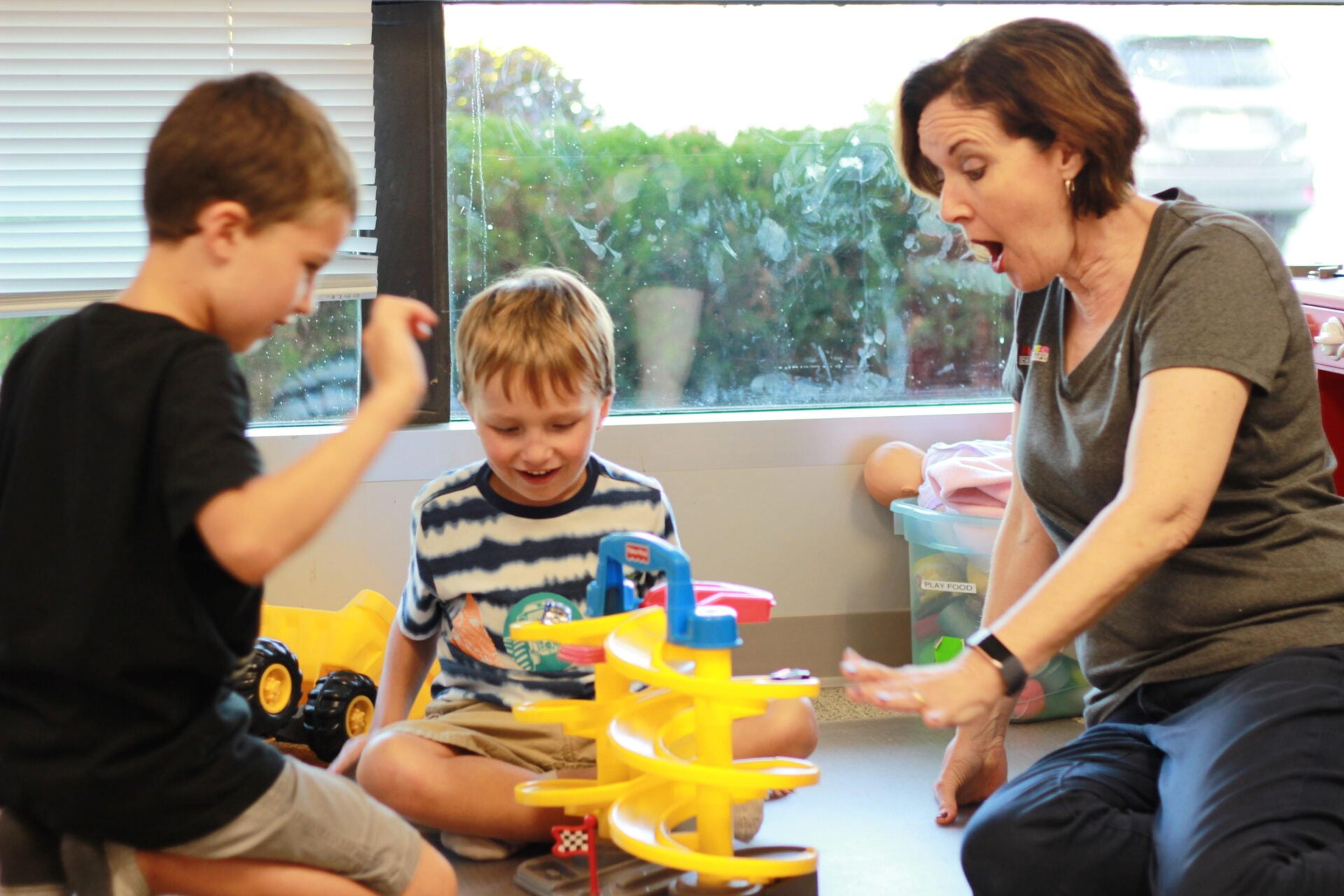 A therapist reacts with delight as two young boys send toy cars down a spiral ramp